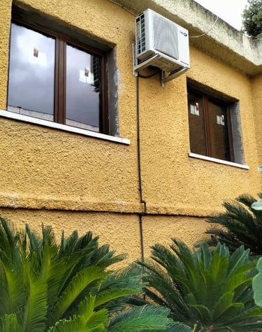 Ventanas de aluminio color marrón en fachada estucada amarilla.