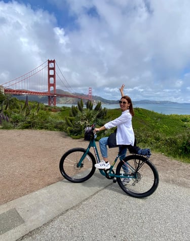 a woman riding a bicycle with a bridge in the background