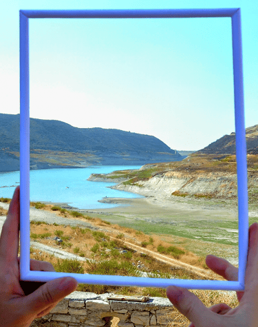 a person holding a picture frame with a picture of a lake