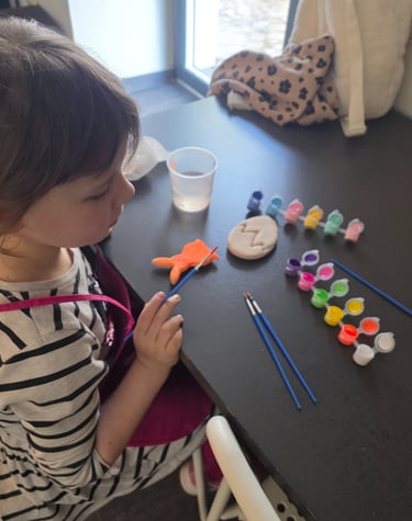 Young girl in a striped shirt painting ceramic Easter eggs and shapes with colorful acrylic paints.