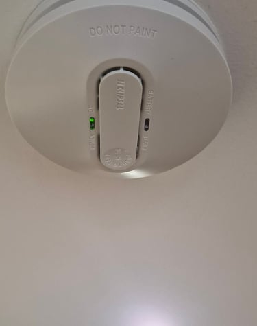 White Clipsal smoke alarm installed on a ceiling with green AC power indicator light.