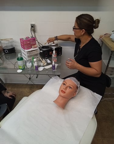 A beauty student practices facial waxing techniques on a mannequin head using a professional wax warmer.