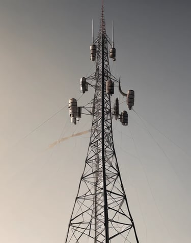 A large telecommunications tower is equipped with numerous antennas and satellite dishes. The structure is complex, with cables and metal components extending outward, set against a background of partly cloudy skies.