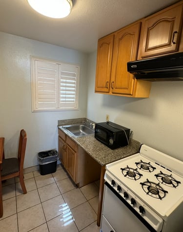 a kitchenette with a stove top, oven, sink, microwave, chair and a table