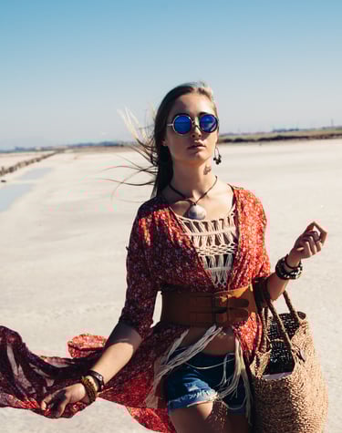 a woman in a red dress and sunglasses walking on a beach