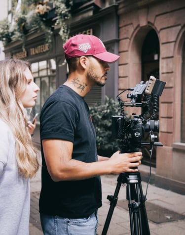 A videographer and director filming a scene with a professional cinema camera on a tripod.