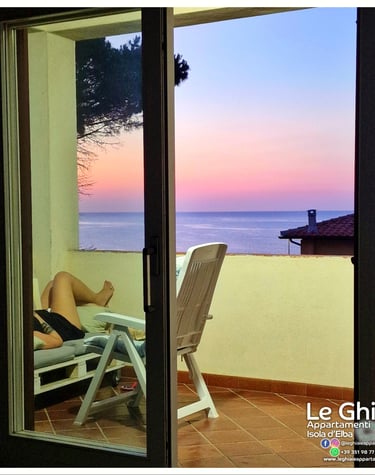 person lying on a chair facing the sea at sunset