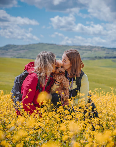 due donne danno un bacio a un cane in campagna tra fiori gialli