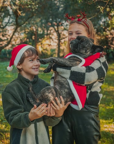 un bambino con un cappello natalizio e una bambina con un cerchietto natalizio abbracciano un cane
