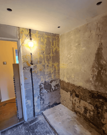 A partially renovated bathroom with stripped walls, exposed plaster, and visible electrical wiring. 