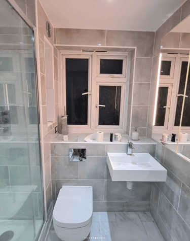 A fully renovated modern bathroom with a sleek glass shower enclosure, wall-mounted toilet, and a mi