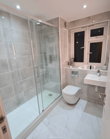 A fully renovated luxury bathroom featuring a large glass walk-in shower, wall-mounted toilet, and a