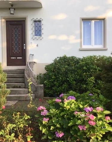 ein Hauseingang mit Treppe und einer Holztür von Büschen und Blumen umgeben