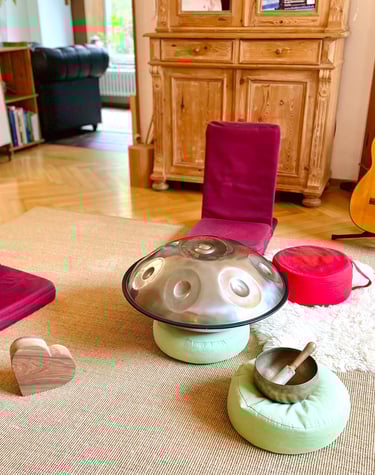 ein heller Raum mit Bodensitzern, einer Handpan und Meditationskissen