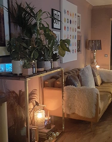 Cozy living room corner with a gold bar cart filled with green houseplants and a glowing candle.