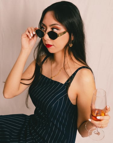a woman in a dress and sunglasses is holding a drink