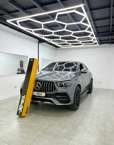 Grey Mercedes-Benz SUV in a detailing studio with XPEL paint protection film box and hexagon LED ceiling lights.
