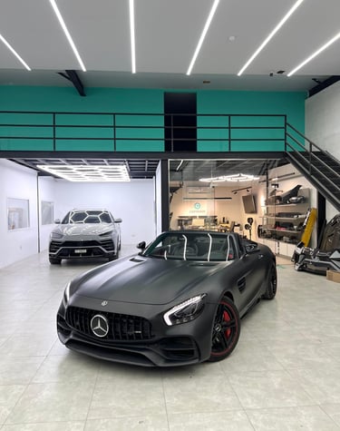 Matte black Mercedes-AMG GT Roadster and silver Lamborghini Urus in a modern luxury car detailing garage.