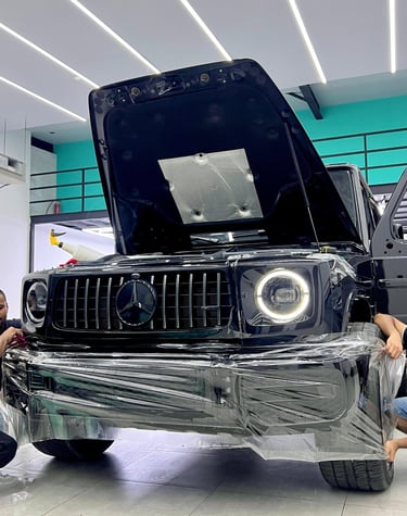 Black Mercedes-Benz G-Wagon receiving a clear paint protection film PPF wrap in a professional detailing shop.