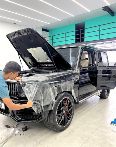 A technician applying clear paint protection film PPF to a black Mercedes-Benz G-Wagon SUV.