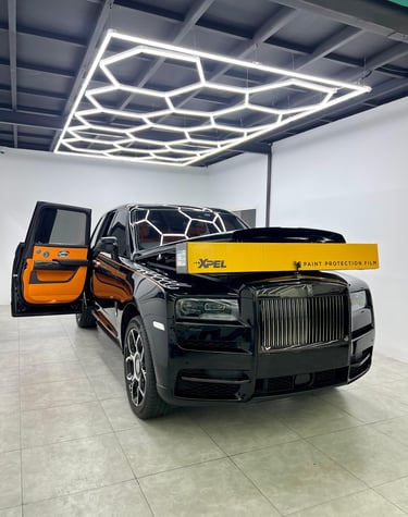 Black Rolls-Royce Cullinan receiving XPEL paint protection film installation in a detailing studio.