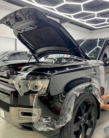 Professional paint protection film application on a black Land Rover Defender in a detailing studio.