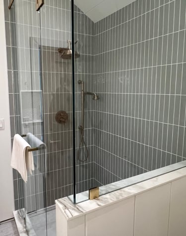 Modern walk-in shower with vertical grey subway tiles, frameless glass enclosure, and bronze hardware.