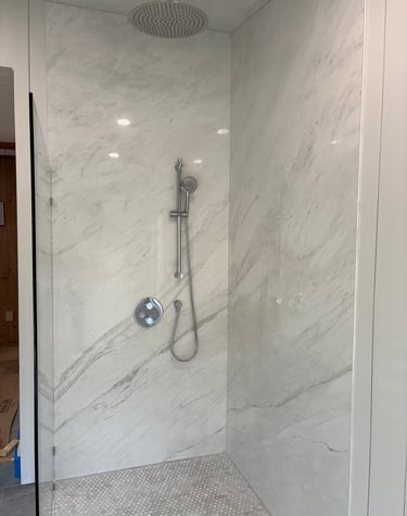 Luxury walk-in shower with white marble wall panels, rain shower head, and chrome handheld sprayer.