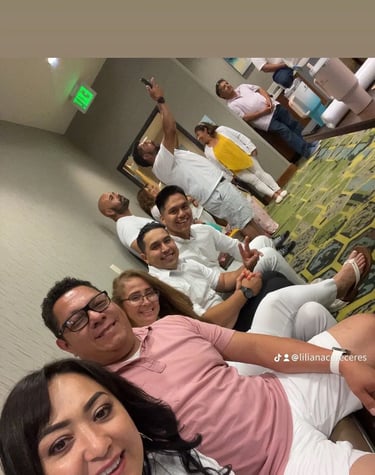 A group of smiling family and friends wearing white and pink shirts gather for a group photo indoors.