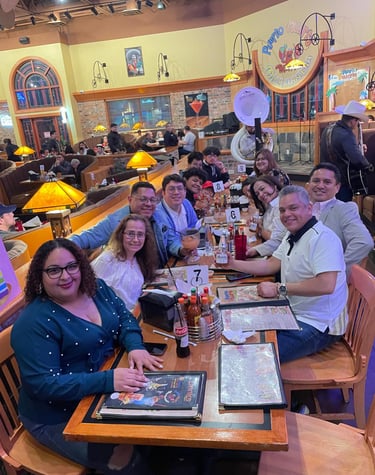 A large group of friends smiling while dining together at a lively Mexican restaurant with live music.