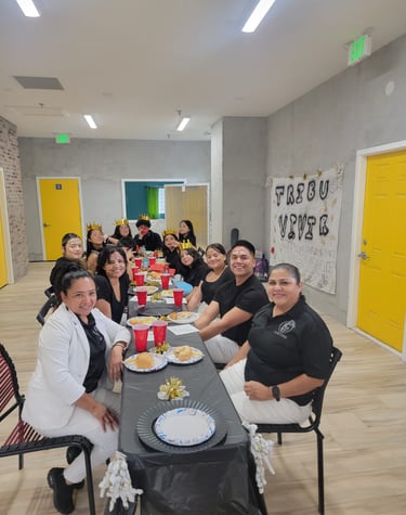 A diverse group of people celebrating at a long banquet table with food, party hats, and festive decor.