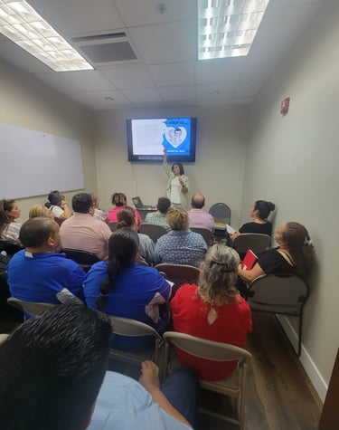 A group of people attending an educational workshop with a woman presenting slides on a digital screen.