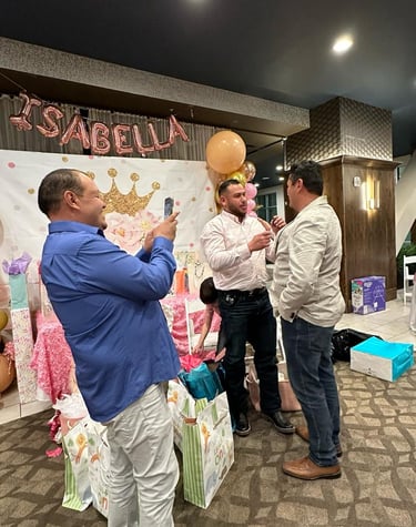 Three men celebrate at a pink princess themed first birthday party with balloons and gifts.