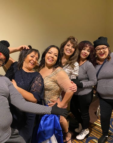 Diverse group of smiling women posing together at a party, including guests in elegant gowns and mimes in striped shirts.