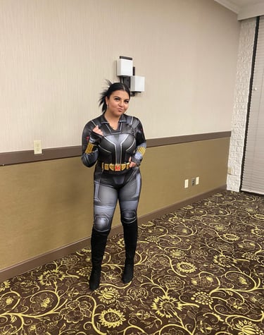 A woman posing in a detailed Black Widow cosplay bodysuit with gold gauntlets and a utility belt.