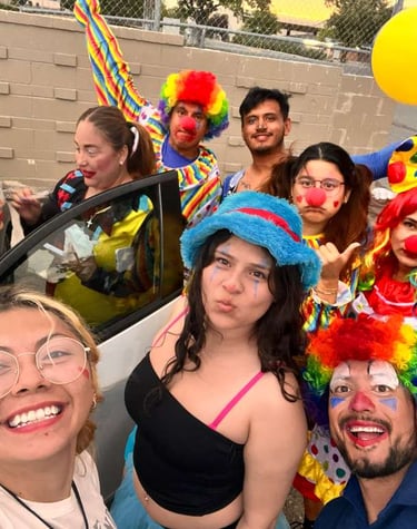 A group of happy friends in colorful clown costumes and wigs taking a fun selfie with bright balloons.
