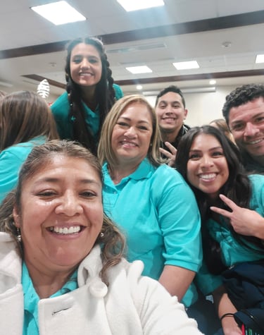 Smiling team members in teal shirts posing for a group selfie during a corporate event.