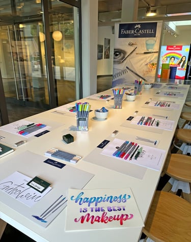 Faber-Castell art workshop table set with colorful Pitt Artist Pens, brush markers, and calligraphy paper.