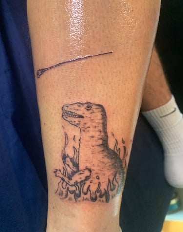 Tatouage dans un style enfantin assumé d'un dinosaure au milieu des flammes par a2c tattoo à Challes