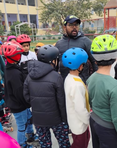 A group of young students in protective helmets and roller skates listen to an instructor at a school skating rink.