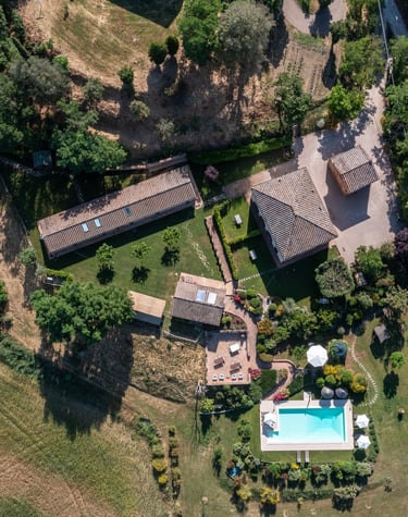 Aerial view of a luxury Italian villa with a blue swimming pool, stone farmhouse, and lush green gardens.