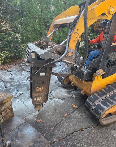 Yellow Cat skid steer with hydraulic hammer attachment breaking up a concrete driveway for demolition.