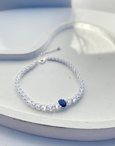 Elegant sterling silver tennis bracelet featuring sparkling clear cubic zirconia and a center blue sapphire stone.