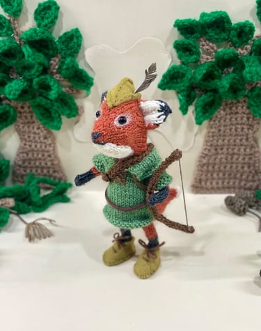 a knitted fox dressed in Disney Robin Hood outfit with a bow and arrows 