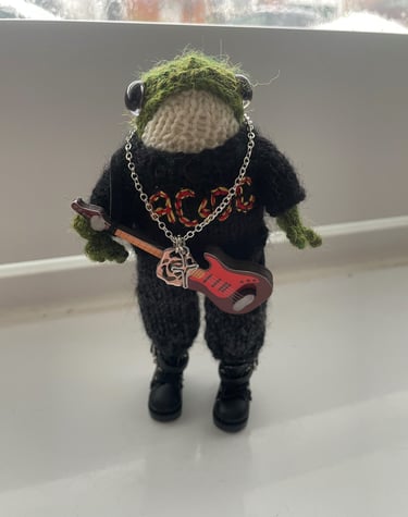 a stuffed frog with a guitar in a knitted jumper with AC/DC on the front 