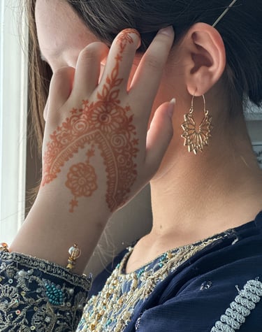 girl with dark hair, wearing a blue beaded tunic, holds hand with henna on it next to her face