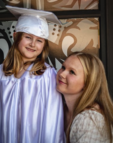 A proud Sister looking at her sibling wearing a white graduation cap and gown.