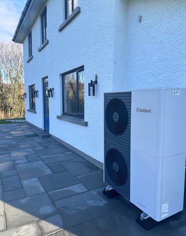 A Vaillant aroTHERM air source heat pump installed on a stone patio outside a white modern home.