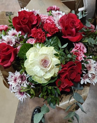 Floral bouquet with red roses, pink daisies, and an ornamental cabbage wrapped floristeria violeta