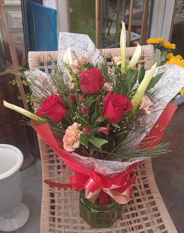A bouquet of red roses, pink carnations, and white lilies in a vase with a red ribbon.